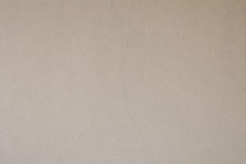 Detailopname van fijne haarscheurtjes in het stucwerk, zoals een spinnenwebpatroon.