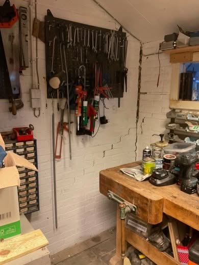 Scheurvorming in het witgeschilderde metselwerk van de garage, naast het gereedschapsbord en de werkbank